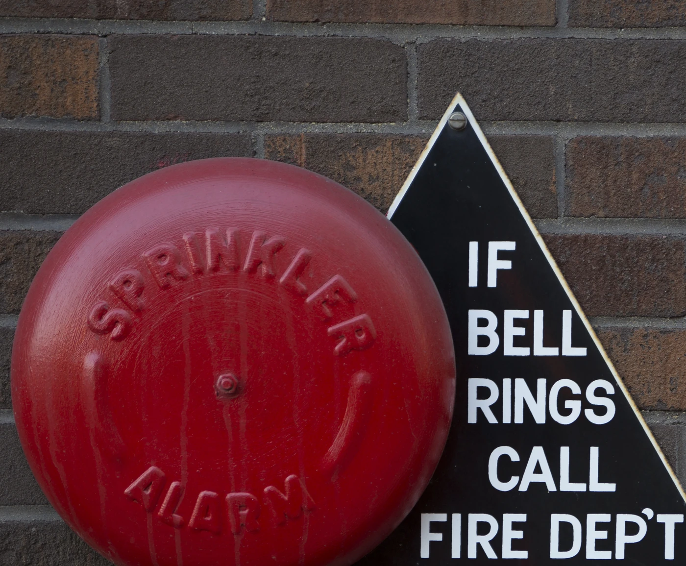 Sprinkler alarm bell and fire watch signage on a building exterior